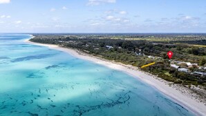 An aerial view of a coastal area with a sandy beach, clear turquoise waters, and a red location marker indicating a specific spot. - Quindy Beach Cottage – Steps to the Bay (Quindalup)