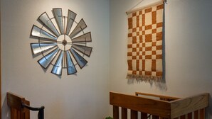 A staircase with a wooden railing, a metal wall decoration, and a checkered fabric hanging on the wall.