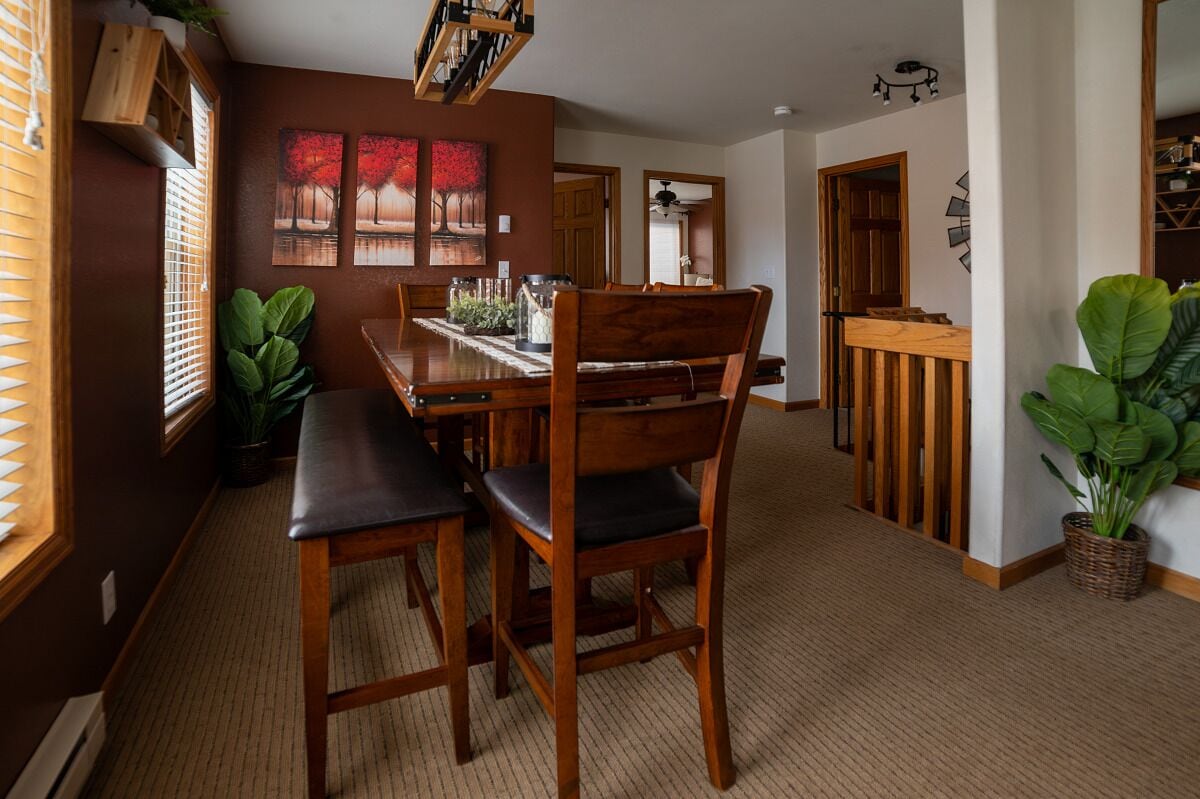 A dining area with a wooden table and chairs, a large plant, and artwork on the wall.