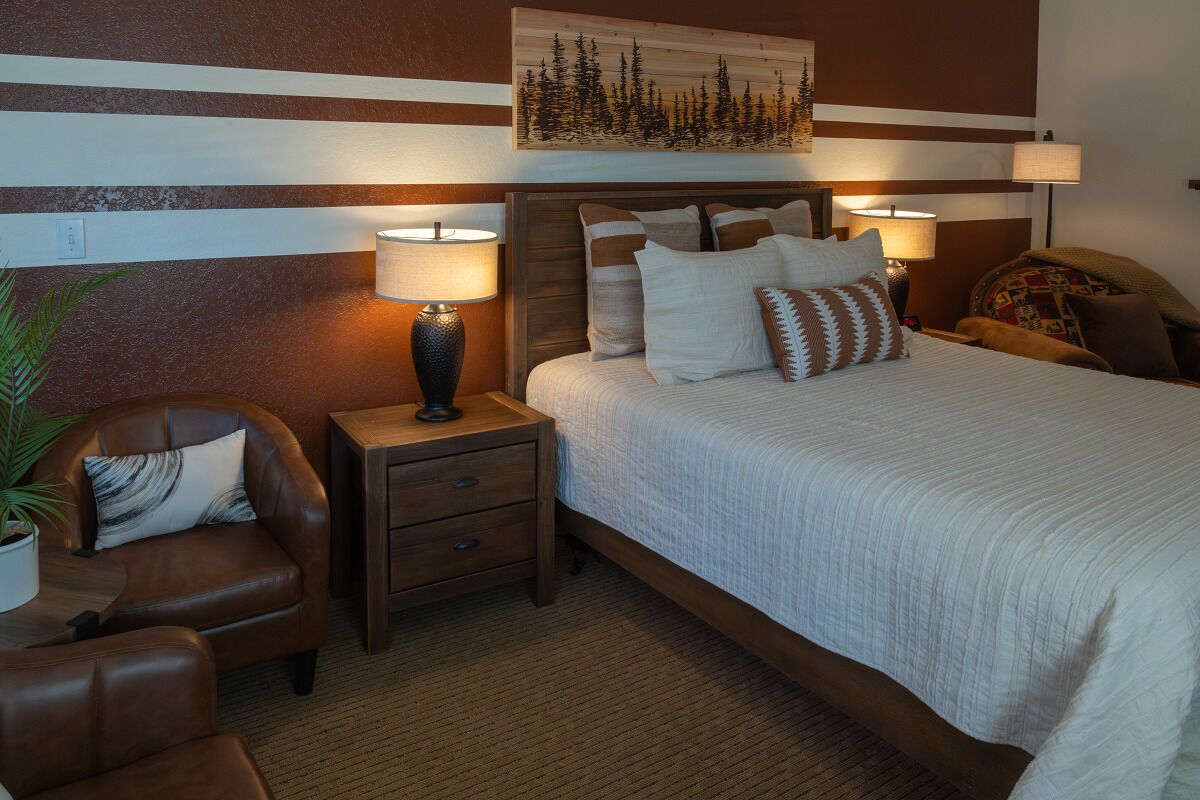 A bedroom with a large bed, two bedside tables with lamps, a brown leather chair, and a wall-mounted painting.