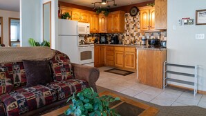 A cozy living room with a patterned sofa, a coffee table, and a kitchen area featuring wooden cabinets, a microwave, and a stove.
