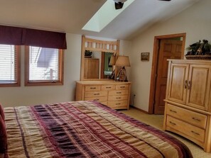 A bedroom with a large bed, wooden dresser, and a mirror. There are windows with blinds, a ceiling fan, and a skylight. - Cascade Three Bedroom Three Bath C03 (Ouray)
