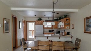 A dining area with a wooden table and chairs, a kitchen with white cabinets and a built-in oven, and a pendant light above the counter. - Cascade Three Bedroom Three Bath C03 (Ouray)