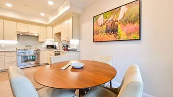 A modern kitchen with white cabinets, a stainless steel oven, and a microwave. There is a round wooden table with two chairs in the foreground.