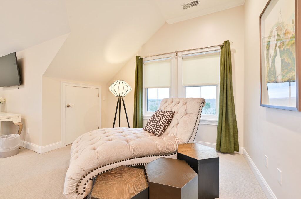 A bedroom with a bed, a bedside table, a lamp, a window with curtains, and a TV mounted on the wall.