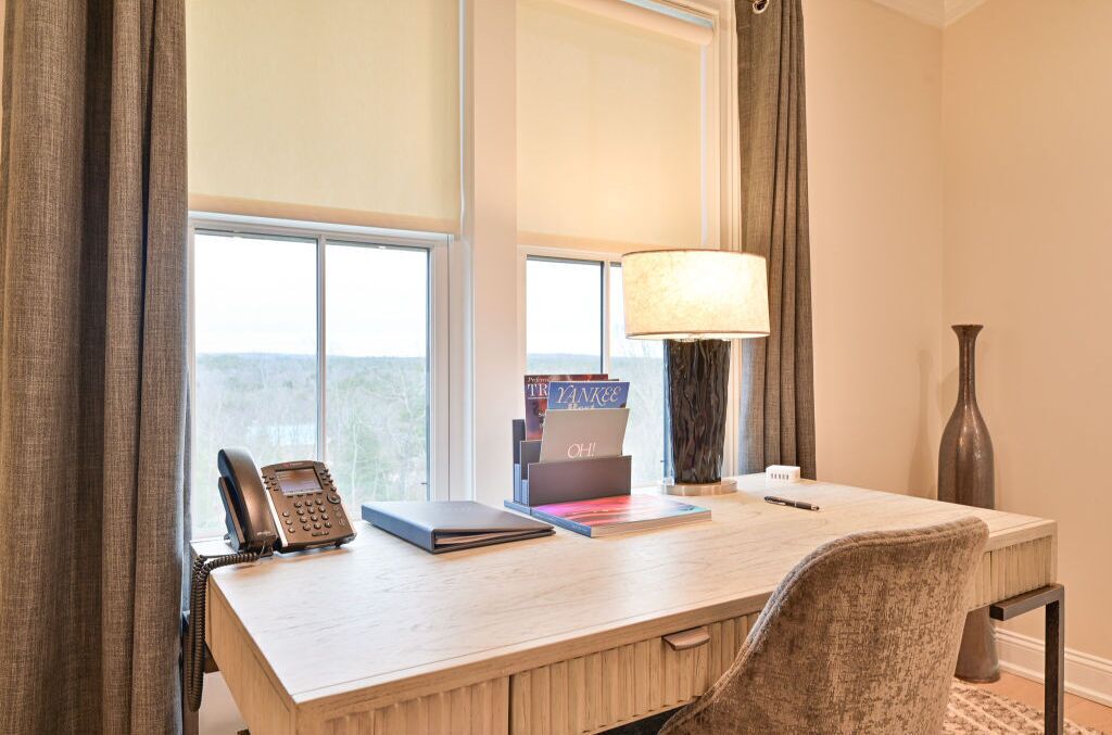 Une chambre d’hôtel équipée d’un bureau, d’un téléphone, d’une lampe et d’une fenêtre avec des rideaux.