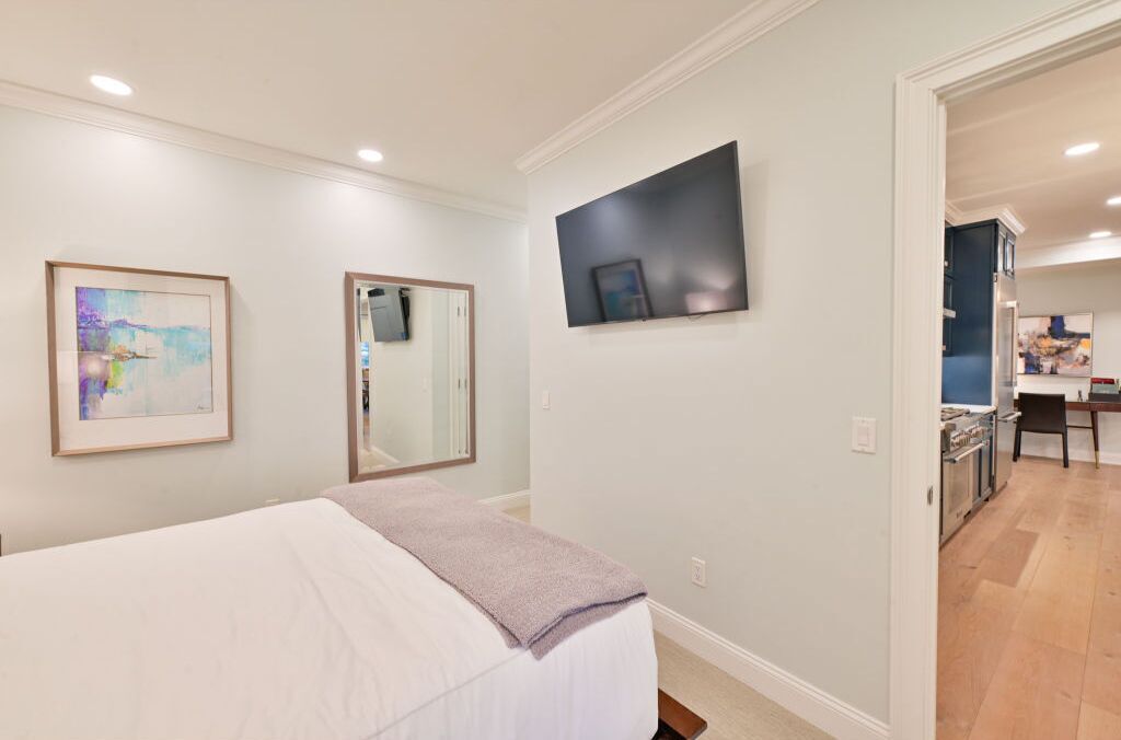A bedroom with a bed, a large mirror, and a flat-screen TV mounted on the wall.