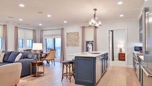 A modern kitchen with a central island, a dining area with a table and chairs, and a living room with a sofa and a lamp. - Exclusive 2BR Suite in Picturesque Woodlands (Richmond)