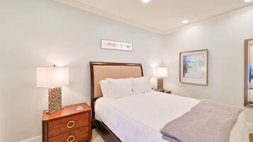A neatly arranged bedroom with a bed, two bedside tables with lamps, a small wooden dresser, and a framed picture on the wall.
