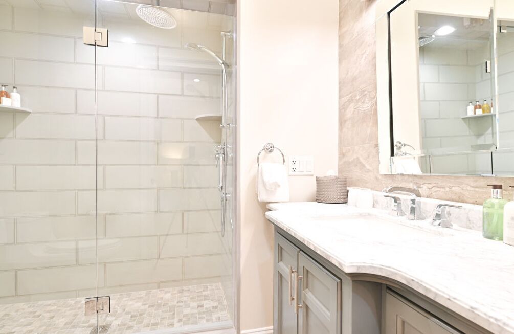 A modern bathroom with a glass-enclosed shower, a marble vanity, and a large mirror.