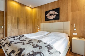 A double bed with a patterned blanket, a wall-mounted artwork of lips, wooden paneling, and bedside lamps.