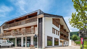 Un edificio moderno con techo plano, balcones y un coche estacionado adelante.