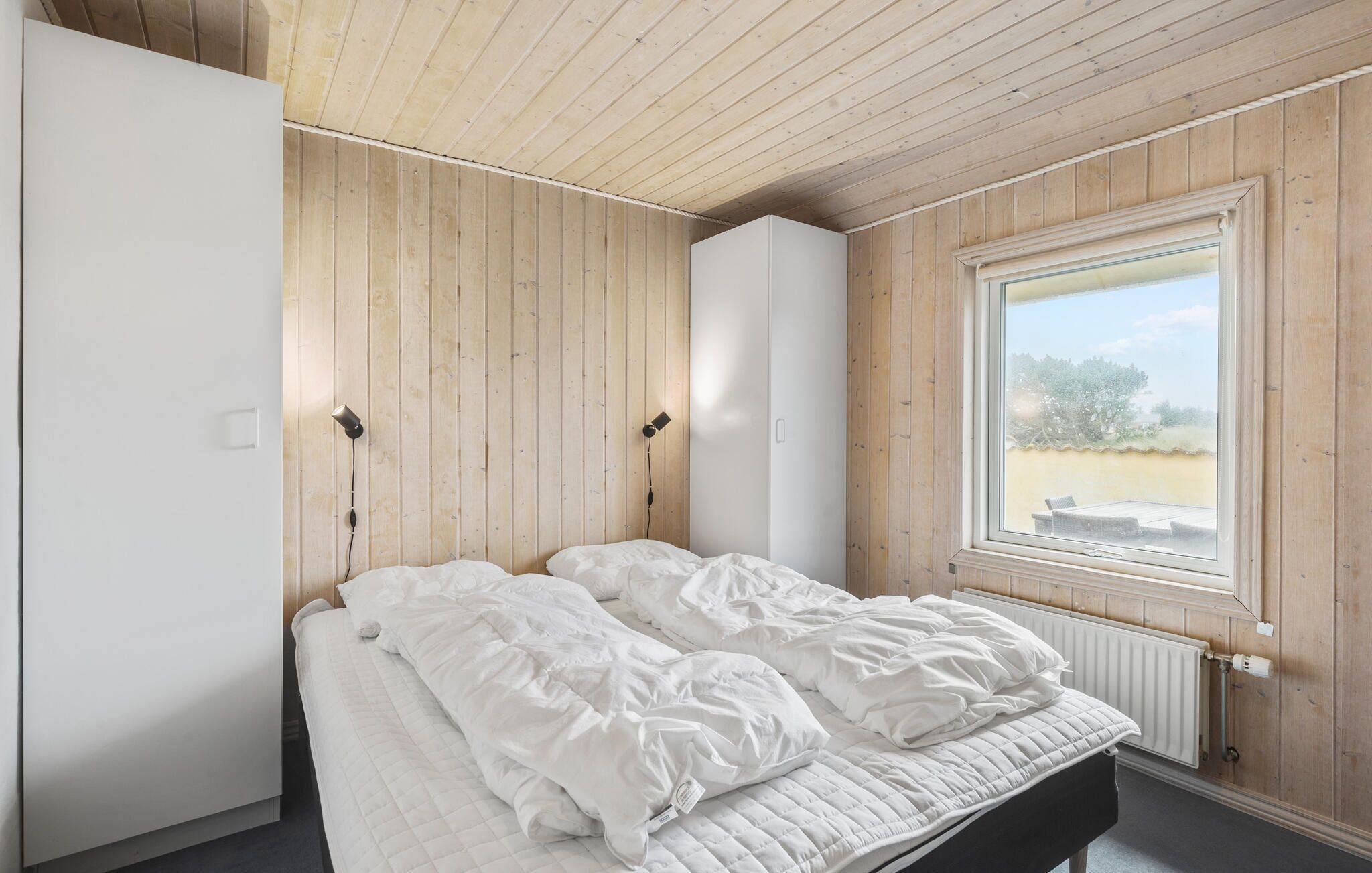 Une chambre à coucher avec un lit, des murs en bois, une fenêtre et un radiateur.