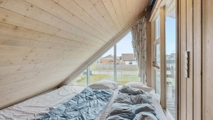 Ett sovrum med ett sluttande tak, en säng med blått och vitt sänglinne och ett fönster med utsikt över ett bostadsområde.