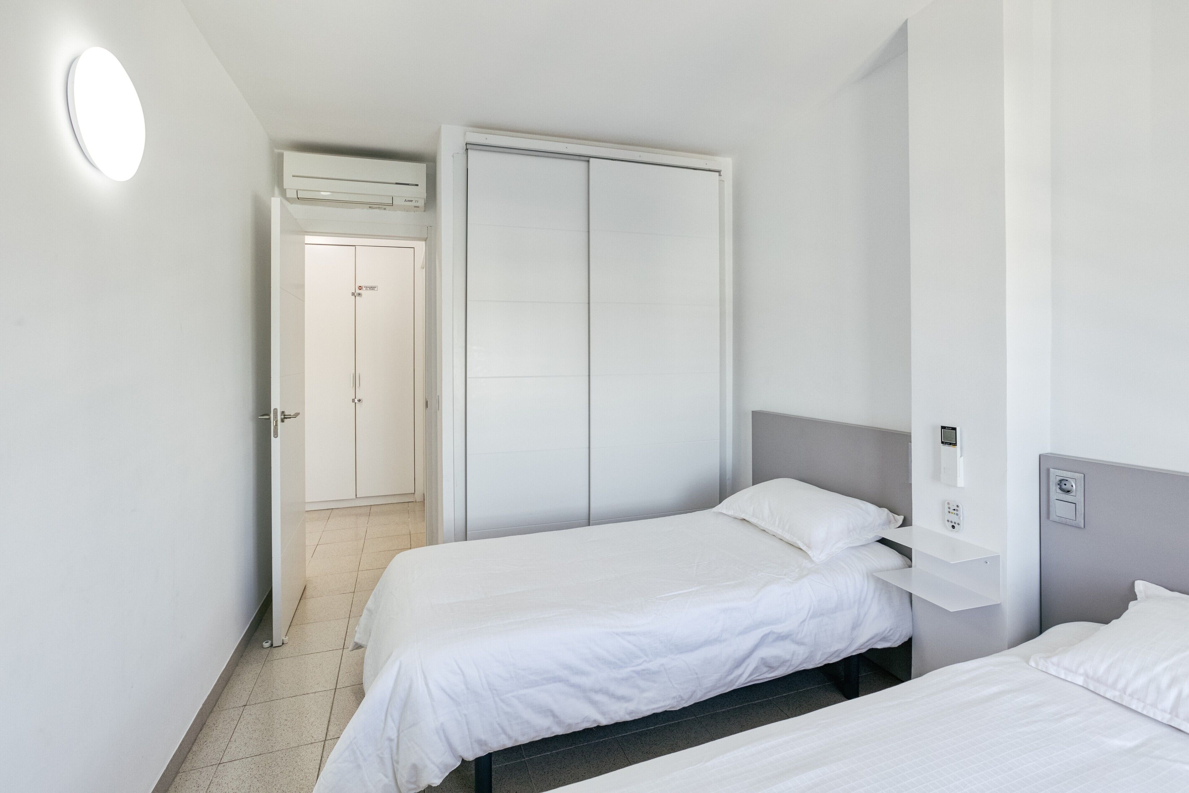 Ein Hotelzimmer mit zwei Betten, einem Kleiderschrank, einer Wandablage und einer Klimaanlage.