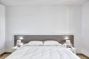 Een net opgemaakt bed met witte lakens, twee nachtkastjes met lampen en een modern hoofdbord.
