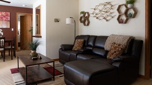 A living room with a dark leather sofa, a coffee table, and a dining area with a wooden table and chairs. - Alpenglow One Bedroom One Bath A18 (Ouray)