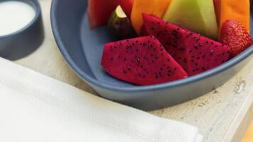 A plate of assorted fruits on a table with a napkin and a glass of orange juice.