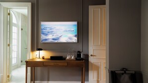 Una stanza con una scrivania in legno, una TV a schermo piatto montata al muro e una porta con portasciugamani.