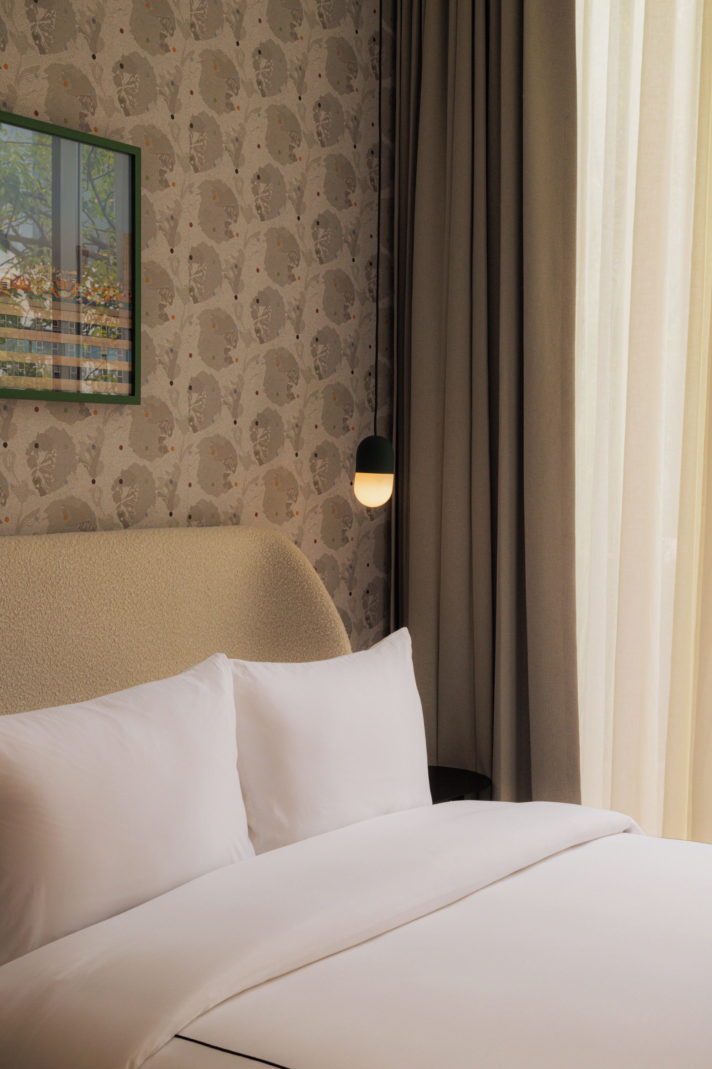 A neatly made bed with white linens, a wall with a floral pattern, and a framed picture above the bed.