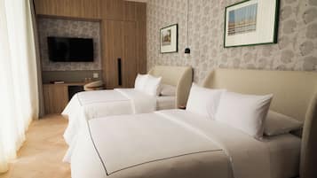 A hotel room with two beds, a flat-screen TV mounted on the wall, a small table with a lamp, and a framed picture on the wall.