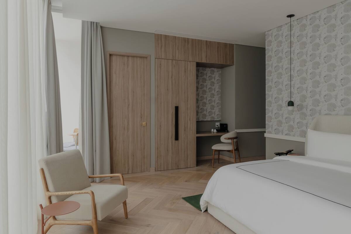 A modern hotel room with a bed, a desk, a chair, and a wardrobe.
