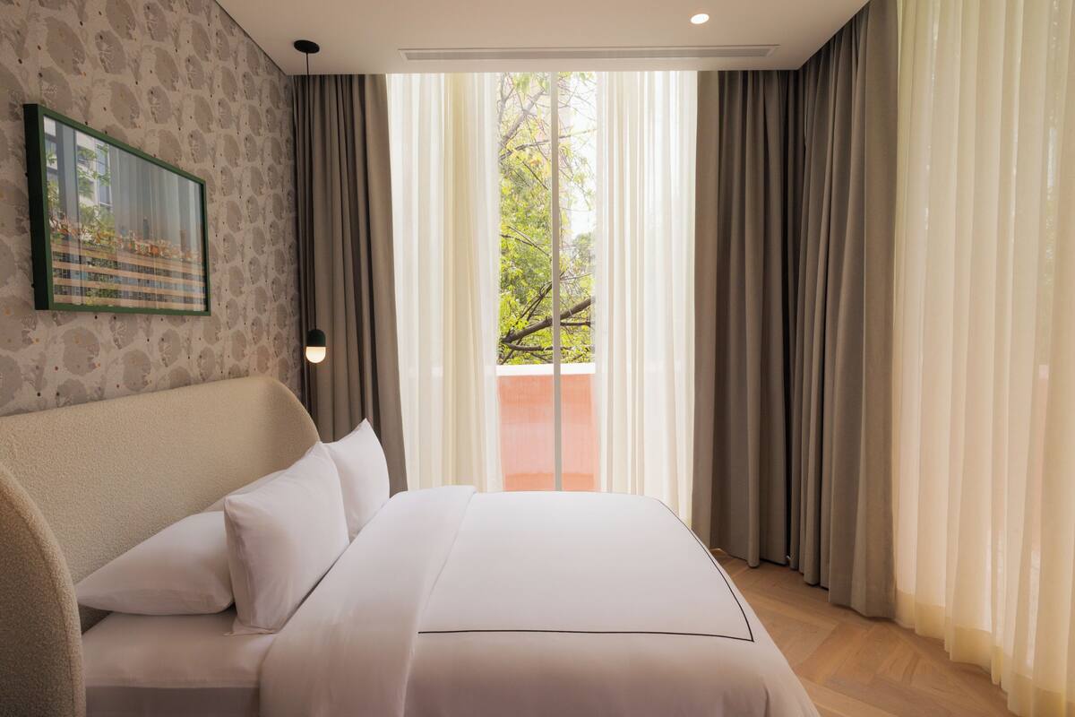 A hotel room with a bed, a headboard, a wall-mounted picture, and a window with curtains.