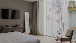 Una camera d'albergo moderna con un letto, una TV, una scrivania con un portatile e una sedia.