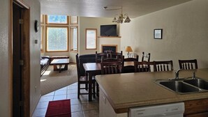A kitchen with a dishwasher, a dining table with chairs, a fireplace, and a TV mounted on the wall. - Cascade Three Bedroom Two Bath C07 (Ouray)