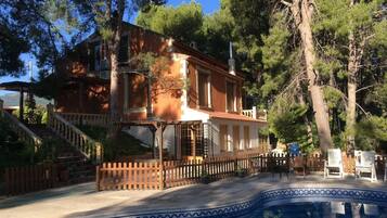 Une maison à deux étages avec une piscine, entourée d’arbres.