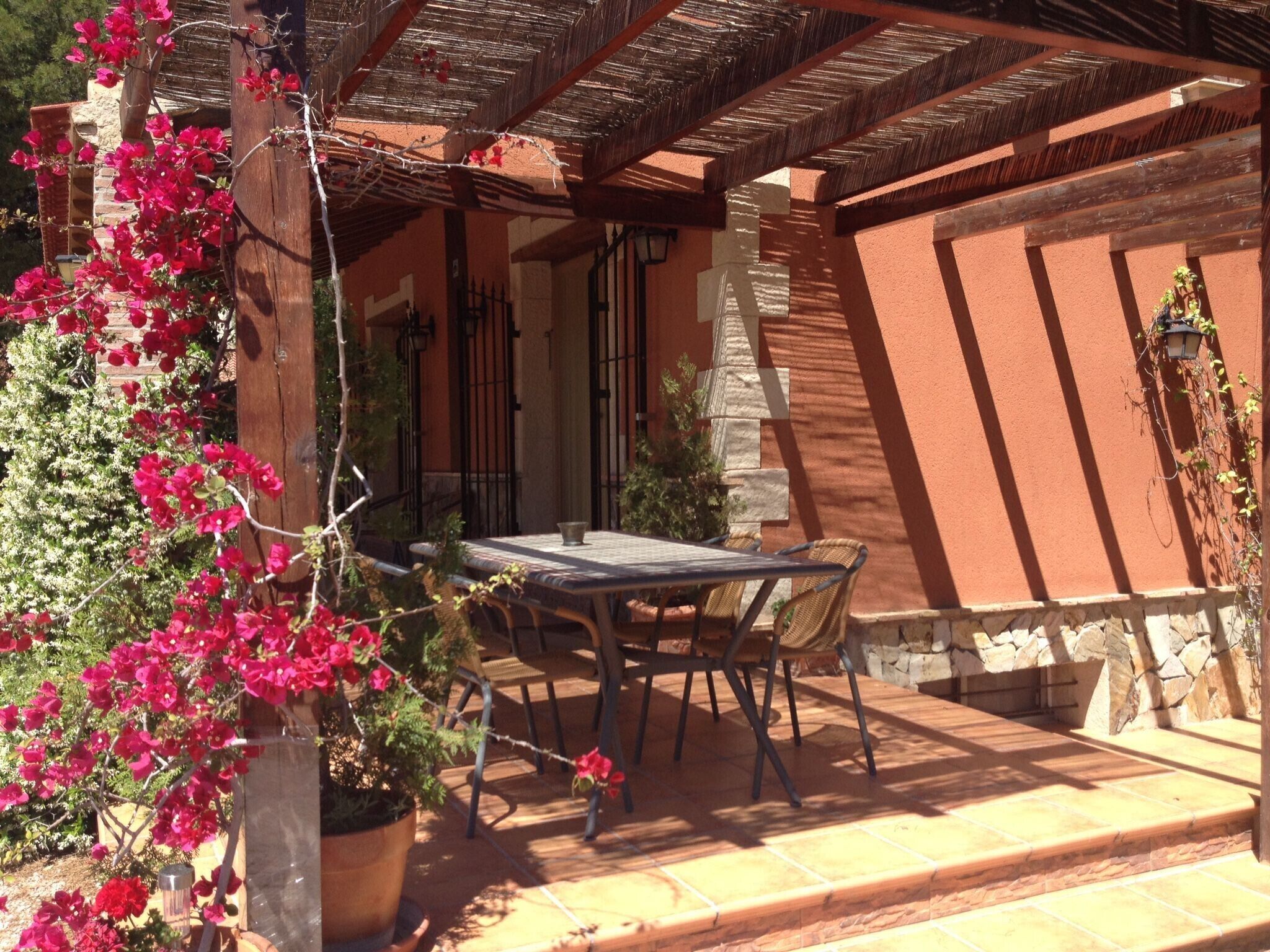 An outdoor patio with a table and chairs, surrounded by a stone wall and a wooden pergola.