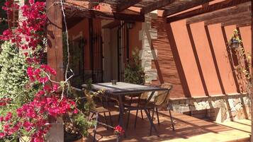 An outdoor patio with a table and chairs, surrounded by a stone wall and a wooden pergola.