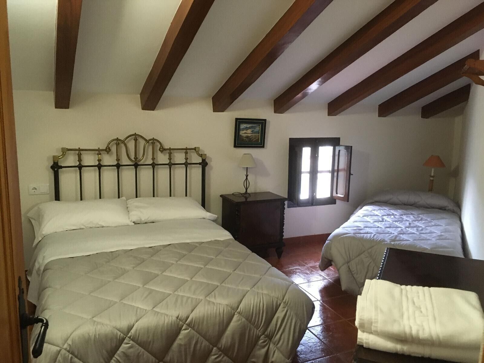 Un dormitorio con dos camas, una mesita de noche, una lámpara, una ventana y un cuadro en la pared.