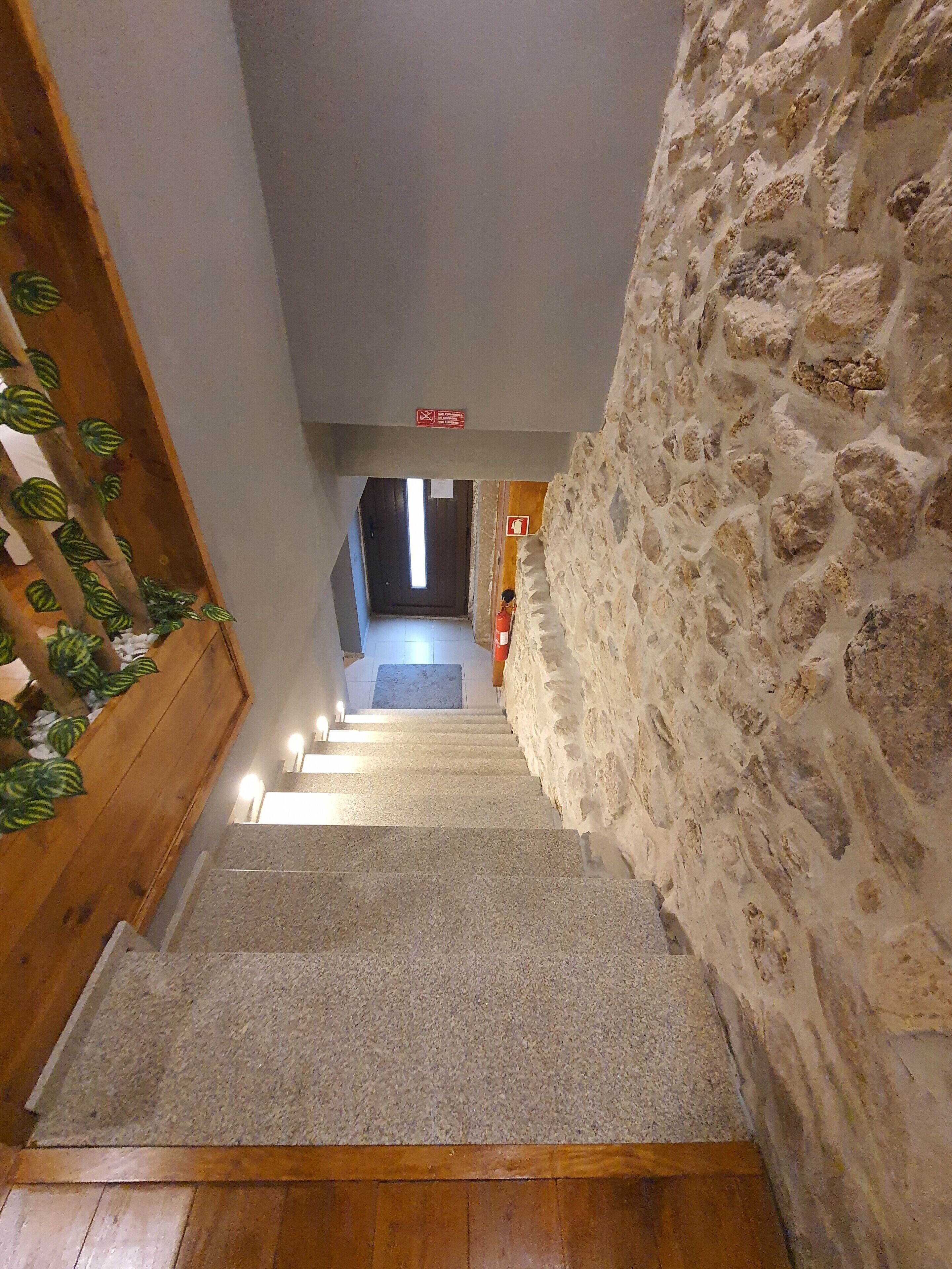 Una escala amb una paret de pedra d'un costat i una barana de fusta de l'altre, que porta a un espai amb finestra i porta a la part superior.