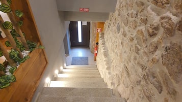 Una escala amb una paret de pedra d'un costat i una barana de fusta de l'altre, que porta a un espai amb finestra i porta a la part superior.
