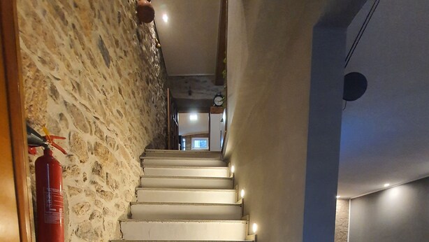 A staircase with a fire extinguisher on the wall, leading to a room with a grey sofa and a patterned rug.