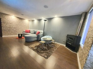 Uma sala de estar moderna com um sofá modular cinza, uma mesinha redonda, um abajur e uma lareira.