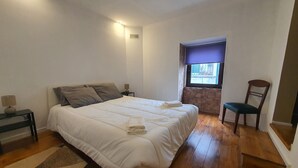 A bedroom with a bed, a nightstand, a chair, a window with a view, and a wooden floor.