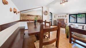 A dining area with a wooden table and chairs, a potted plant, and a view of the kitchen and outside. - Apartment 'Appartamento Rupestre  2.0' with Private Terrace, Private Garden and Wi-Fi (Manerba del Garda)