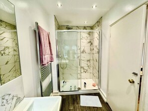 Ein Badezimmer mit einer Duschkabine, einem weißen Waschbecken und einer Wand mit Marmorfliesen.