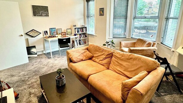 En stue med sofa, sofabord, bogreol og skrivebord med computer.