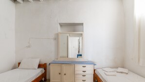 A bedroom with two single beds, a wooden dresser with drawers, a mirror, and a white wall. - Marino's Country House 1 Apartment with Sea View, Wi-Fi, and Air Conditioning (Sifnos)