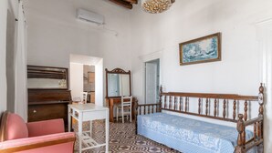 A room with a patterned floor, a wooden bench, a pink chair, a white table, a mirror, and a painting on the wall. - Marino's Country House 1 Apartment with Sea View, Wi-Fi, and Air Conditioning (Sifnos)