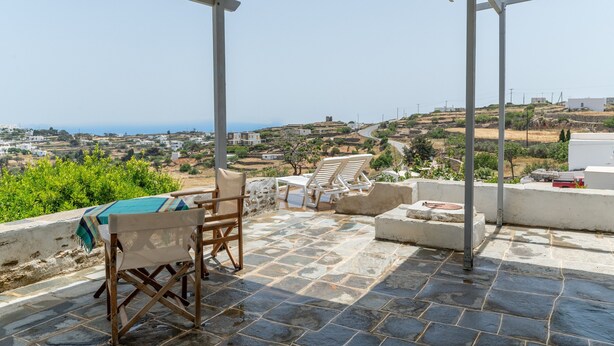 A terrace with stone flooring, a table with a tablecloth, two chairs, and a view of a hilly landscape. - Marino's Country House 1 Apartment with Sea View, Wi-Fi, and Air Conditioning (Sifnos)