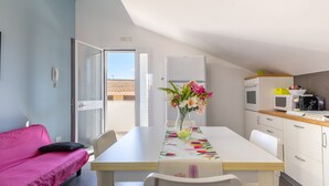 A compact kitchen with a dining table, chairs, a pink sofa, and a view through an open door.