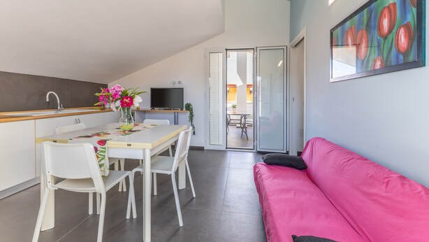 A modern kitchen with a dining table and chairs, a pink sofa, and a painting on the wall.