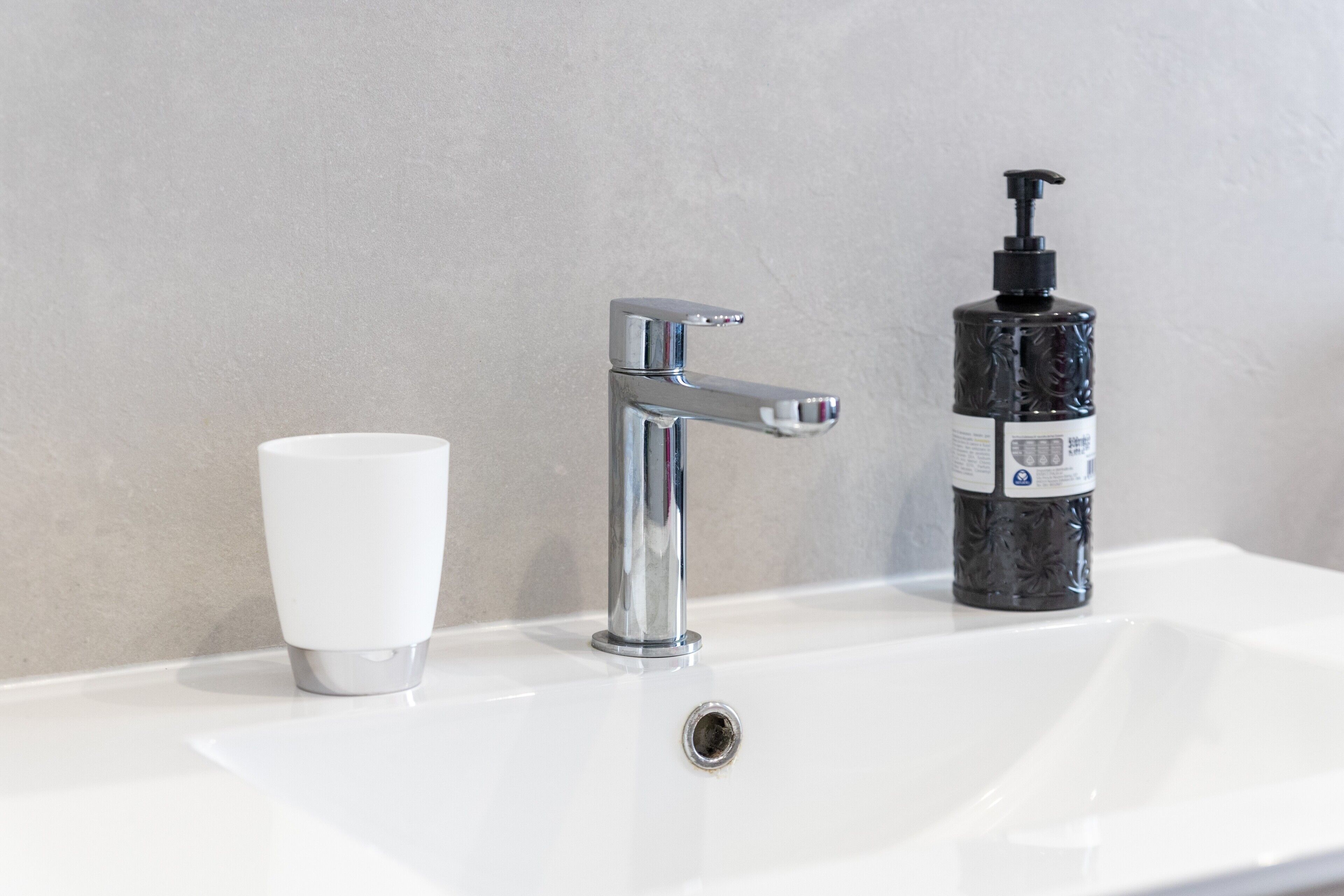 A bathroom sink with a chrome faucet, a white cup, and a black bottle with a pump dispenser.