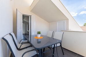 Ein Balkon mit einem Glastisch und Stühlen, einem Blumentopf und Blick auf den Himmel.