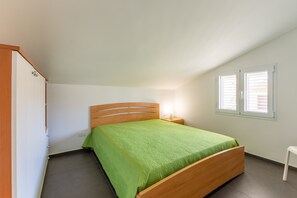 Ein Schlafzimmer mit einem hölzernen Bett, einem Nachttisch, einem Fenster mit Jalousien und einer Tür.