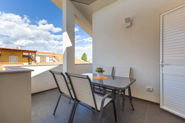 Ein Balkon mit Tisch und Stühlen, einem Blumentopf und Blick auf Gebäude und Himmel.